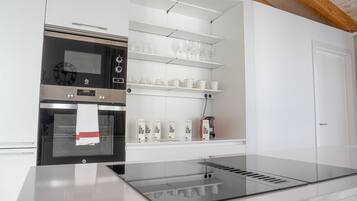 Una cocina moderna con horno empotrado, cafetera y estantes con tazas y recipientes.