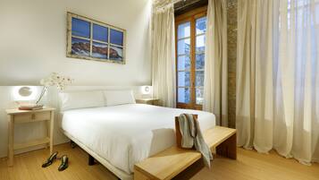 A neatly arranged bedroom with a large bed, bedside tables with lamps, a bench, and a window with curtains.