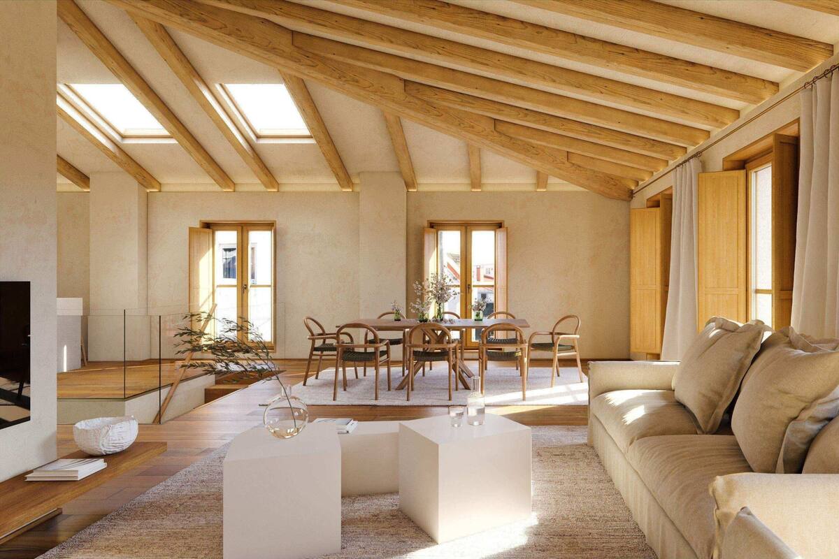 Ein geräumiges Wohnzimmer mit hohen Decken, Holzbalken, einem Essbereich mit Stühlen und Tisch sowie einer Couch mit Kissen.