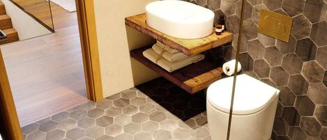 Un baño moderno con un lavabo redondo, estantes de madera y baldosas hexagonales.
