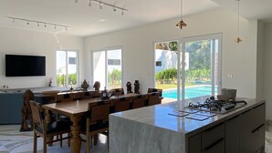 A modern kitchen with a large island, a dining area with wooden chairs, and a view of a swimming pool.