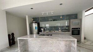 A modern kitchen with a marble island, stainless steel appliances, and a grey backsplash.
