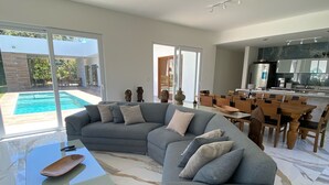 A modern living room with a sectional sofa, a glass coffee table, and a dining area with wooden chairs.
