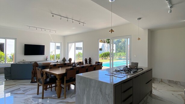 A spacious kitchen with a marble island, a dining area with a large table, and a TV mounted on the wall.