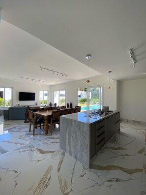 A spacious kitchen with a marble island, a dining area with a large table, and a TV mounted on the wall.