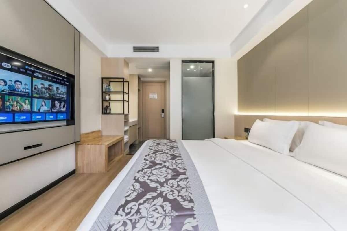 A modern hotel room with a large flat-screen TV, a neatly made bed, and a wooden bench.