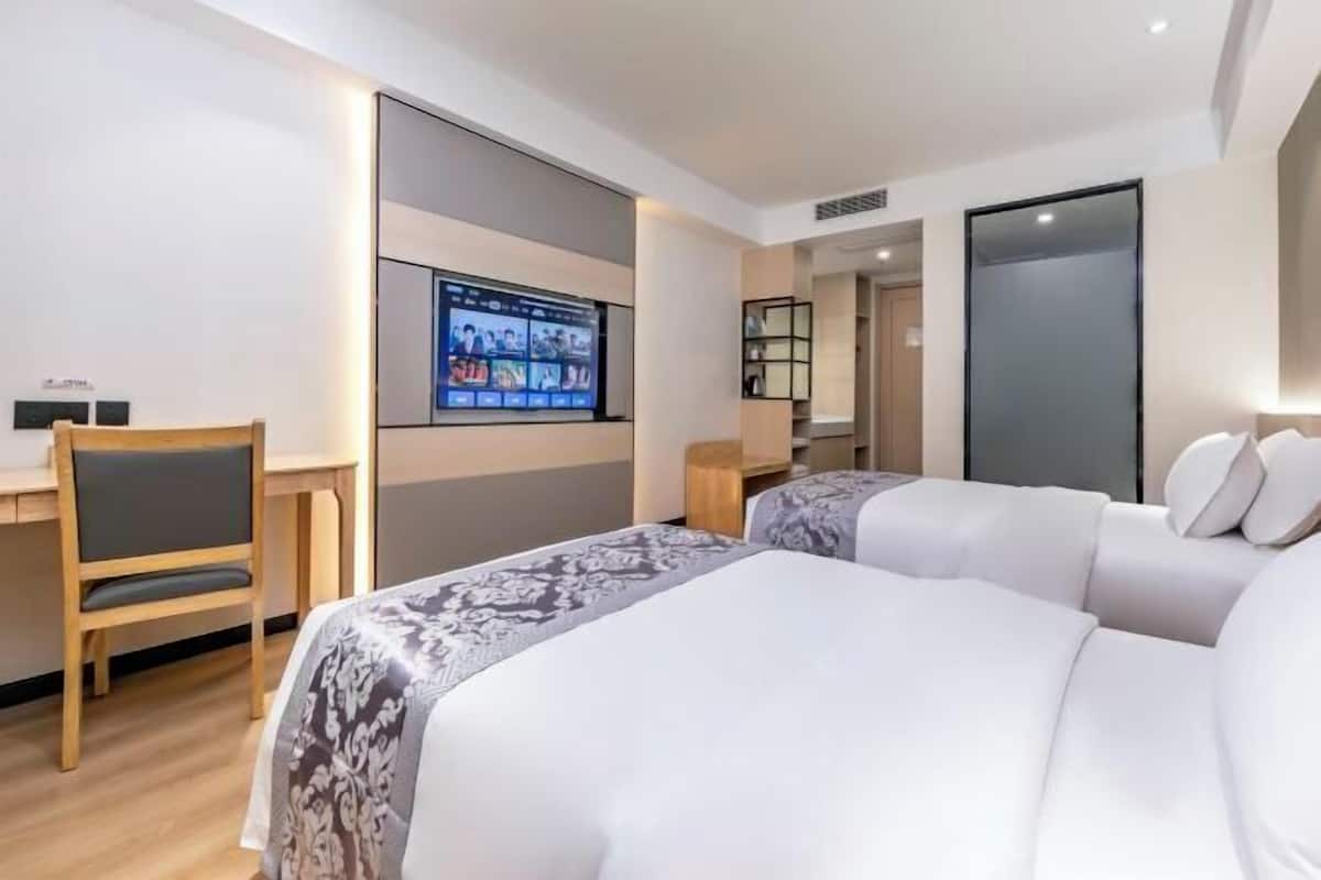 A modern hotel room with two beds, a desk, and a large TV screen displaying a video conference.