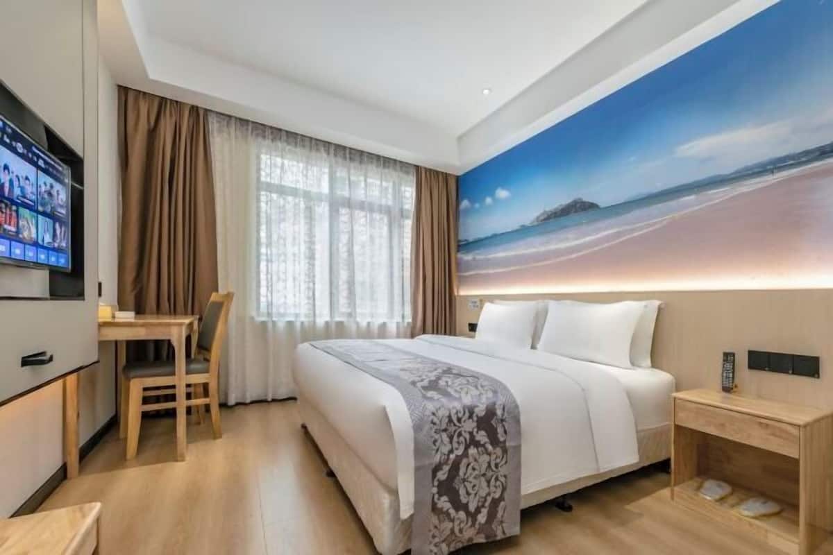A hotel room with a bed, a desk, a chair, a TV, and a painting of a beach scene.