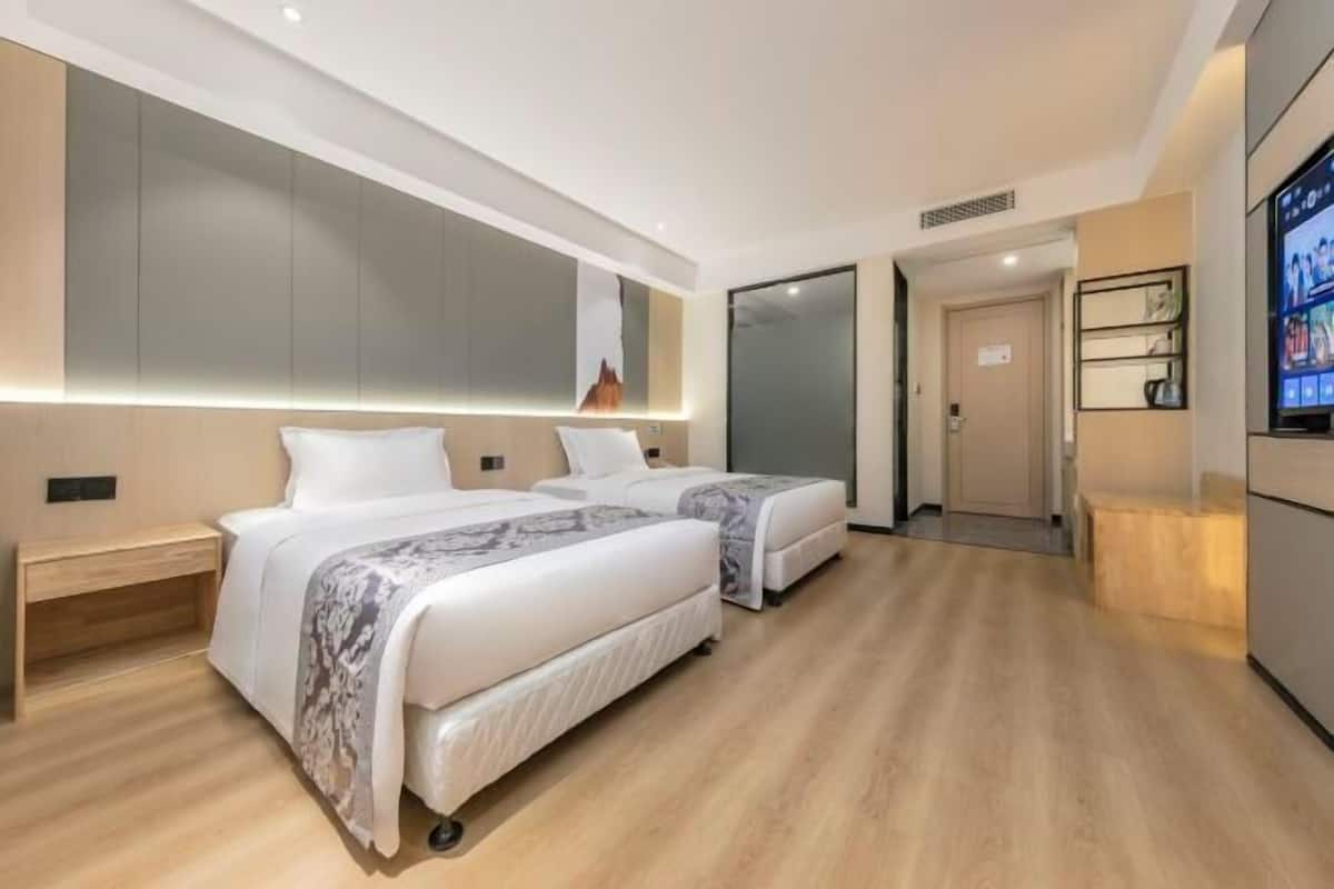 A modern hotel room with two beds, a large mirror, a TV, and a wooden floor.