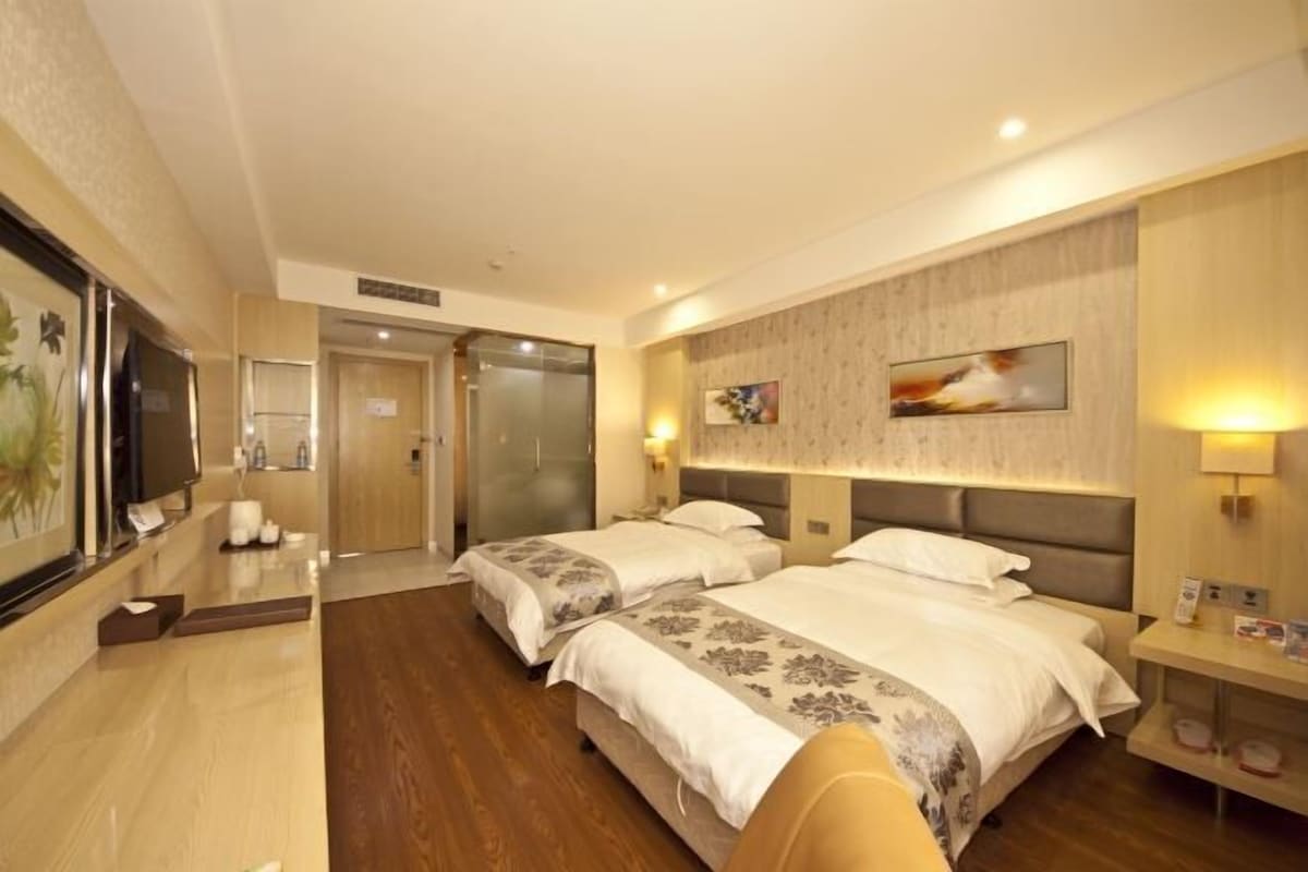A hotel room with two beds, a TV, a desk, and a bathroom.