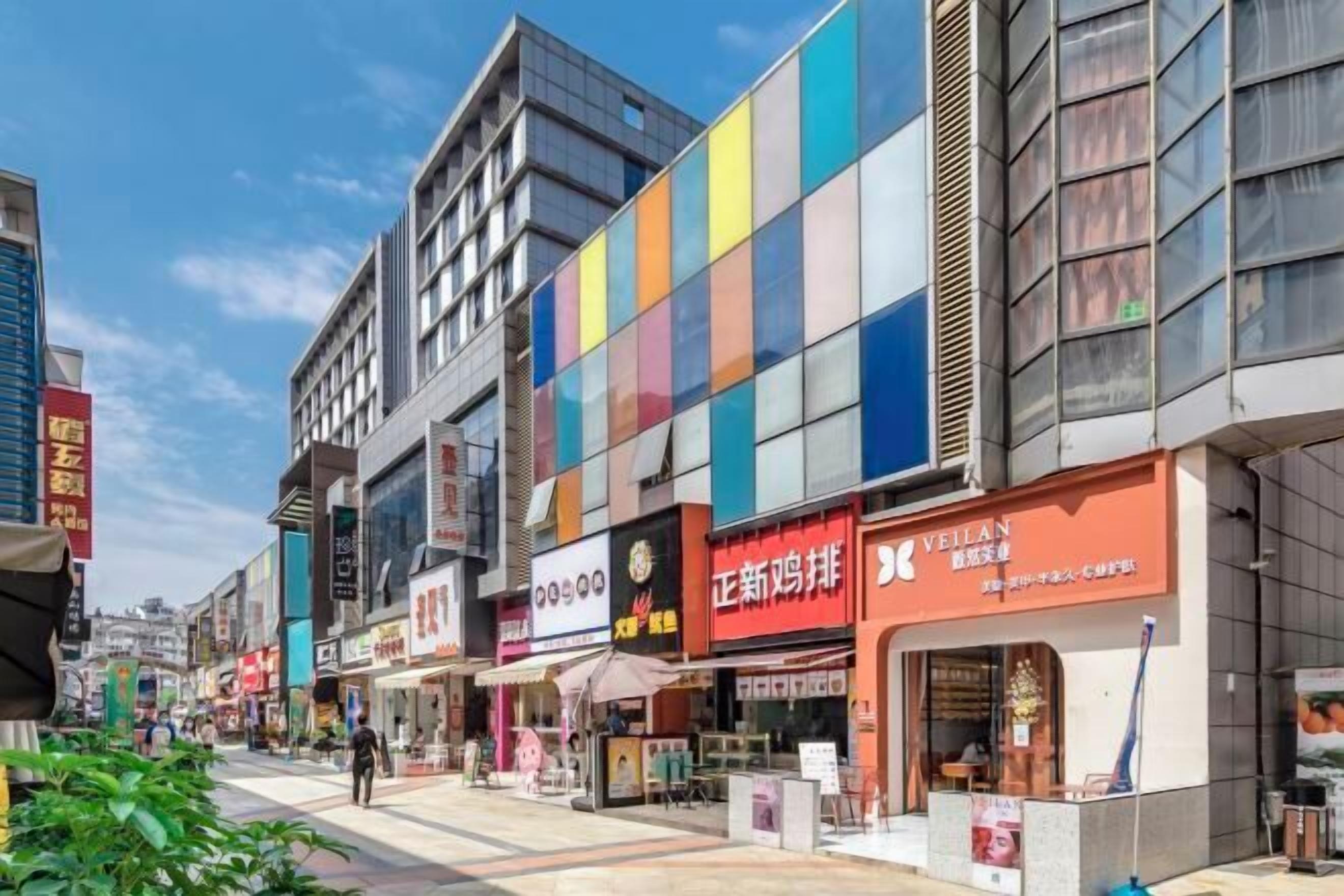 A street view with modern buildings, storefronts, and a pedestrian walkway.