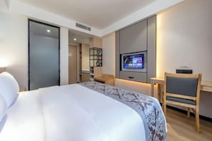 A hotel room with a bed, a desk, a chair, a TV, and a wardrobe.