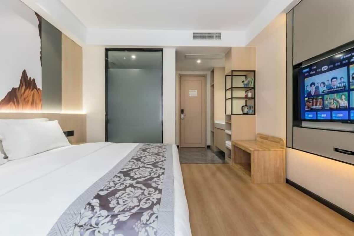A modern hotel room with a bed, a TV, a wooden bench, and a wall-mounted shelf.