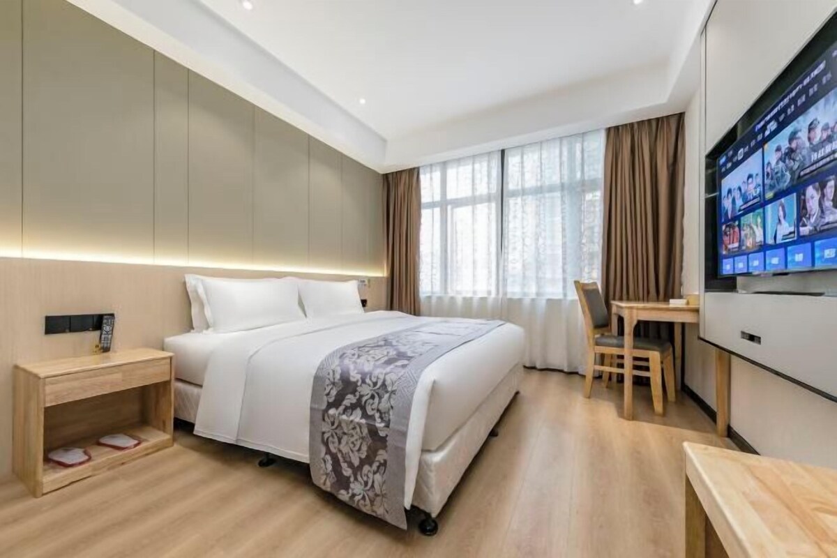 A hotel room with a bed, bedside table, TV, and a desk with a chair.