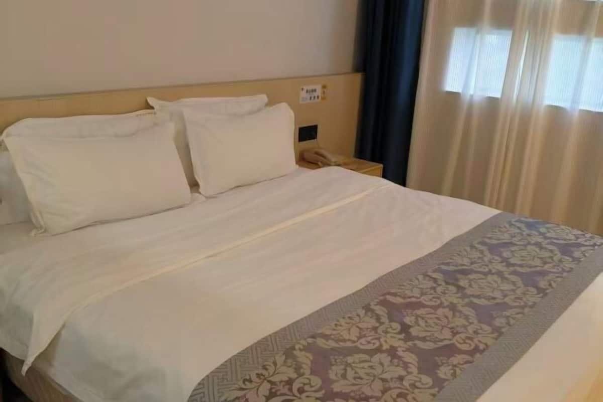 A hotel room with a bed, a nightstand, a telephone, and a window with curtains.