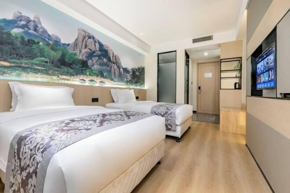 A hotel room with a large bed, a smaller bed, a TV, and a mural of a landscape.