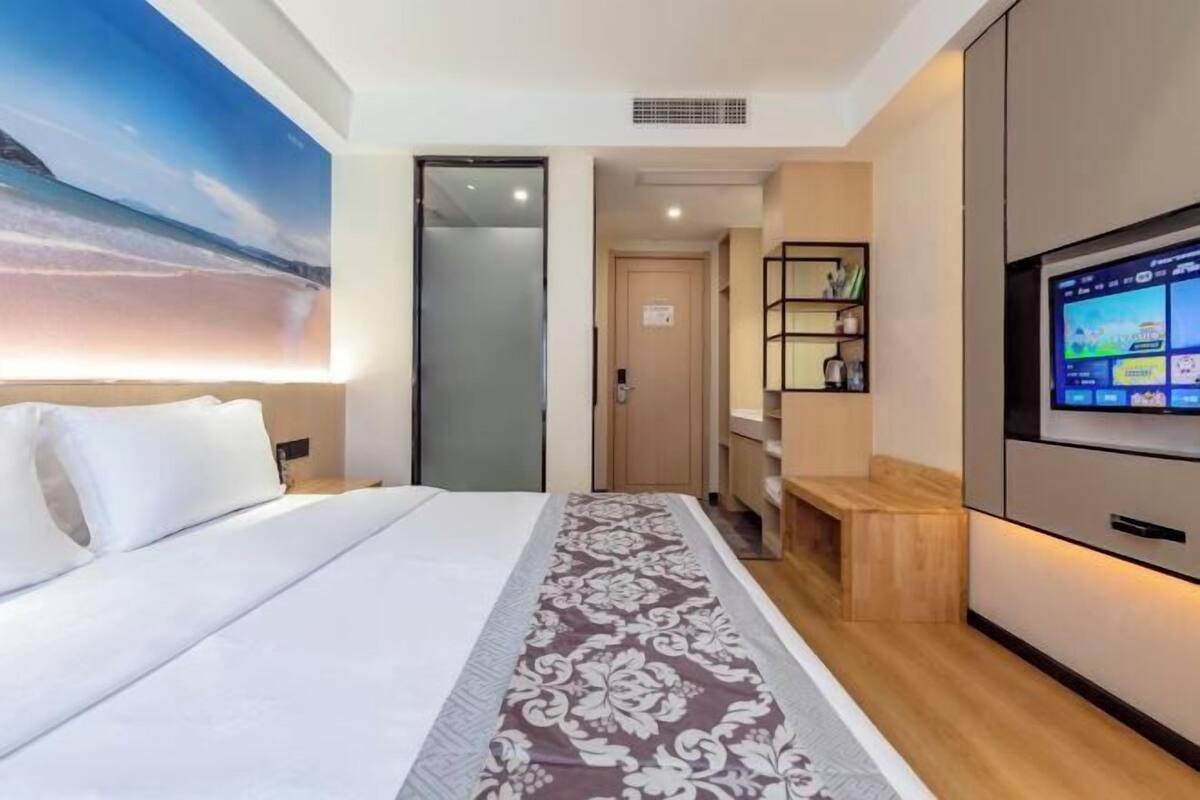 A hotel room with a bed, a TV, a bookshelf, and a painting on the wall.