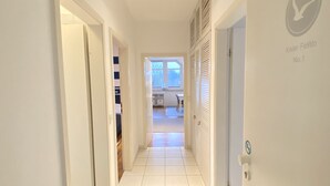 A hallway with white tiled floors and doors, leading to a room with a window and a view of the outdoors. - Kieler FeWo No.1, kieler-fewo de (Kiel)