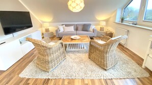 A modern living room with a sofa, two wicker chairs, a coffee table, and a flat-screen TV mounted on the wall. - Kieler FeWo No.1, kieler-fewo de (Kiel)