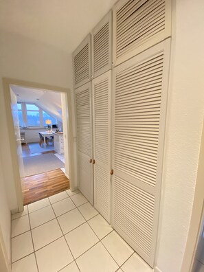 Un pasillo con suelo de baldosas blancas, una sección de suelo de madera y vistas a una habitación con escritorio y silla.