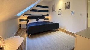 A bedroom with a sloped ceiling, a bed with a dark headboard, bedside lamps, and a small desk with a chair. - Kieler FeWo No.1, kieler-fewo de (Kiel)