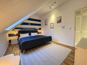 Un dormitorio con cama, escritorio, silla, alfombra estampada y una lámpara en el techo.