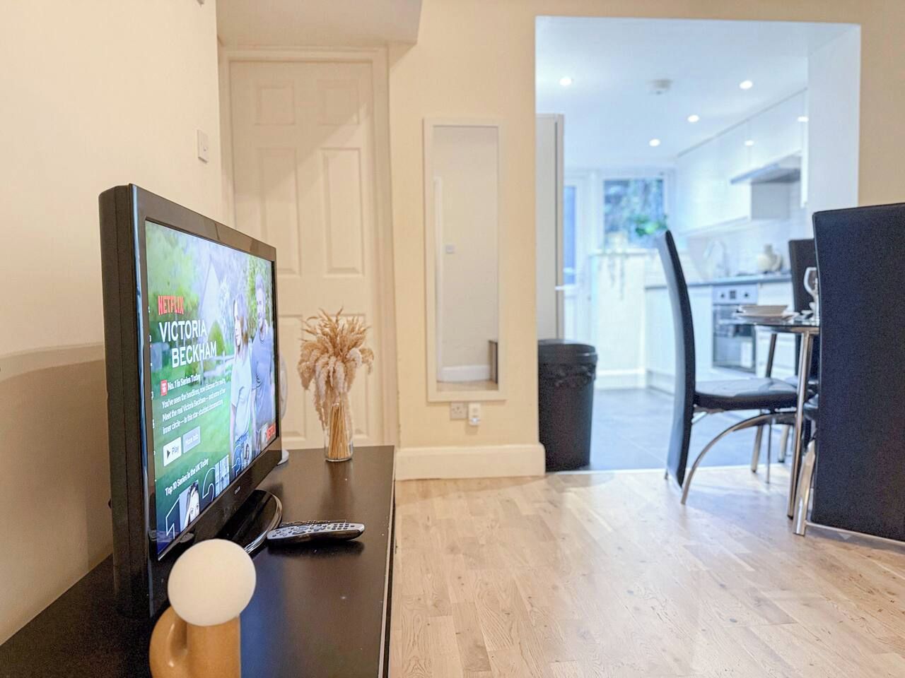 A modern living room with a flat-screen TV, a remote control, and a decorative vase on a wooden table.