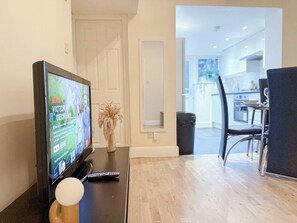 A modern living room with a flat-screen TV, a remote control, and a decorative vase on a wooden table.