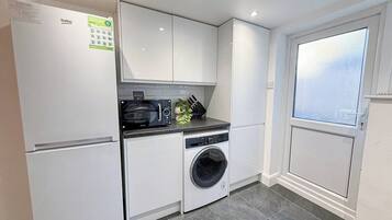 A compact kitchen with a refrigerator, microwave, oven, and washing machine.