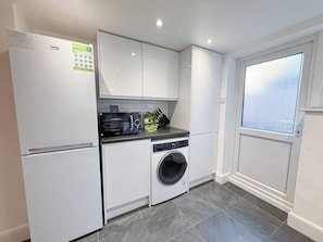 A compact kitchen with a refrigerator, microwave, oven, and washing machine.
