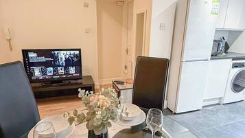A modern living room with a dining area, a television displaying a show, and a kitchen with a washing machine.