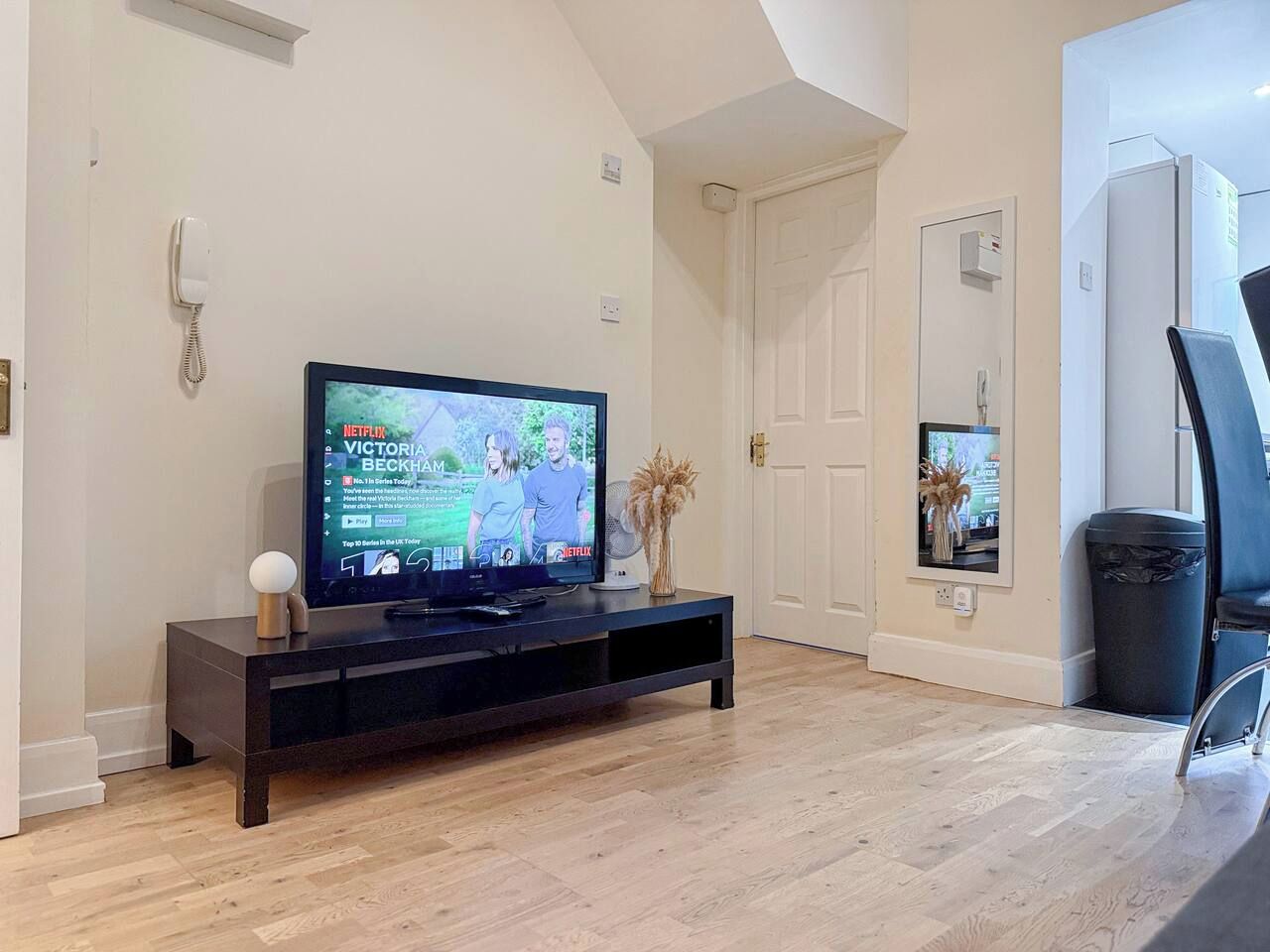 A modern living room with a flat-screen TV on a dark wooden stand, a white door, and a small window with a view.