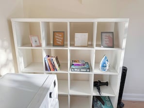Un estante blanco con varios objetos, incluyendo libros, una cita inspiradora enmarcada y un pequeño electrodoméstico azul.
