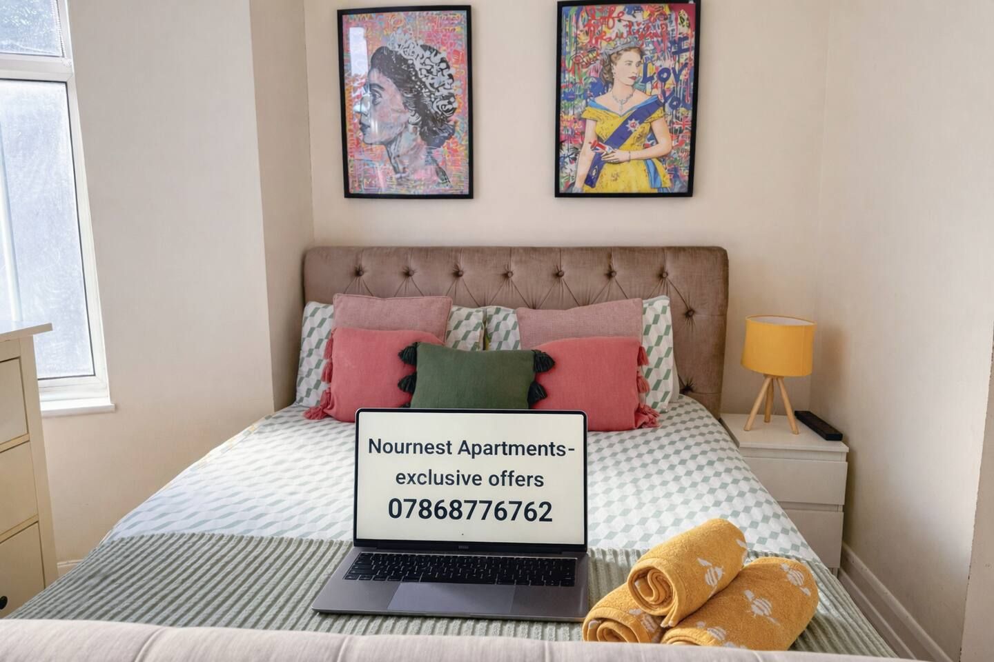 Ein Schlafzimmer mit einem Bett, einem Laptop, einem Nachttisch und zwei gerahmten Kunstwerken an der Wand.