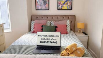 Ein Schlafzimmer mit einem Bett, einem Laptop, einem Nachttisch und zwei gerahmten Kunstwerken an der Wand.