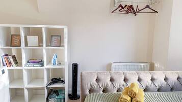 A bedroom with a tufted headboard, a white shelving unit with books and a black speaker, and a radiator.