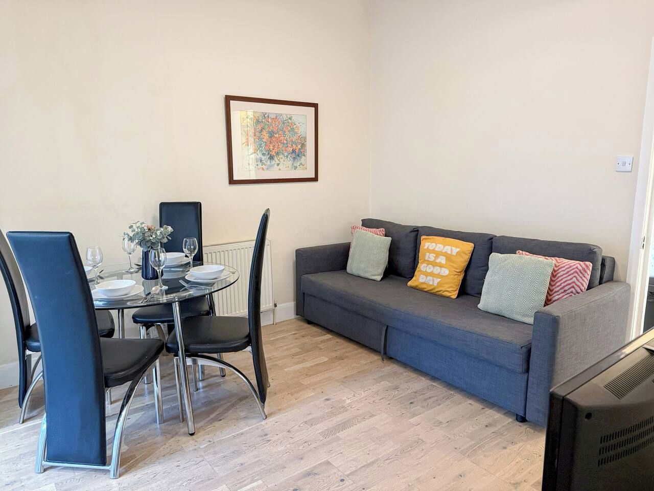 Een woonkamer met een grijze bank, zwarte stoelen, een eettafel met borden en glazen, en een lijst met een foto aan de muur.