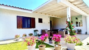 A white building with a covered patio area, potted plants, and outdoor furniture.