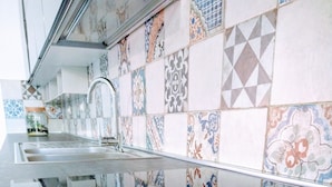 A kitchen with a modern design, featuring a stainless steel sink and a backsplash with various geometric and floral tile patterns.