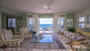 A living room with a glass coffee table, wicker chairs, a floral sofa, and a view of the ocean through open shutters. - Sweet's Spot at The Truman Annex in Key West (Key West)
