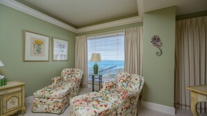 A room with two floral armchairs, a small table, a lamp, and a view of the sea through a window with curtains. - Sweet's Spot at The Truman Annex in Key West (Key West)