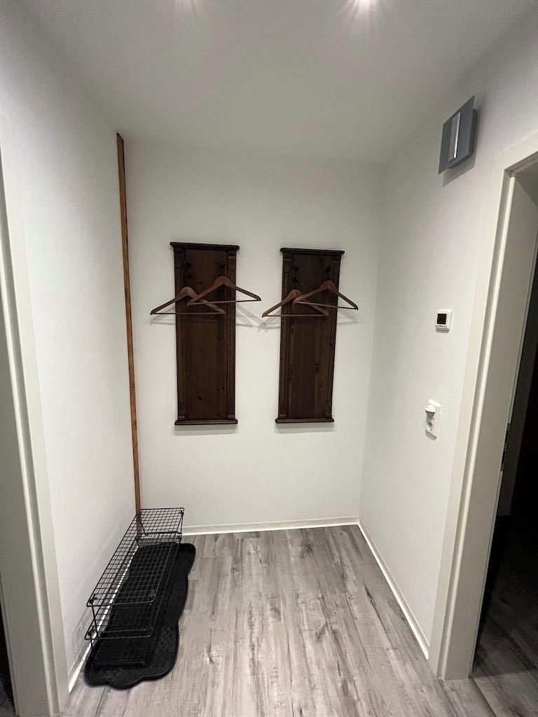 Une petite pièce bien éclairée, avec deux fenêtres en bois, un étagère en métal et une porte.