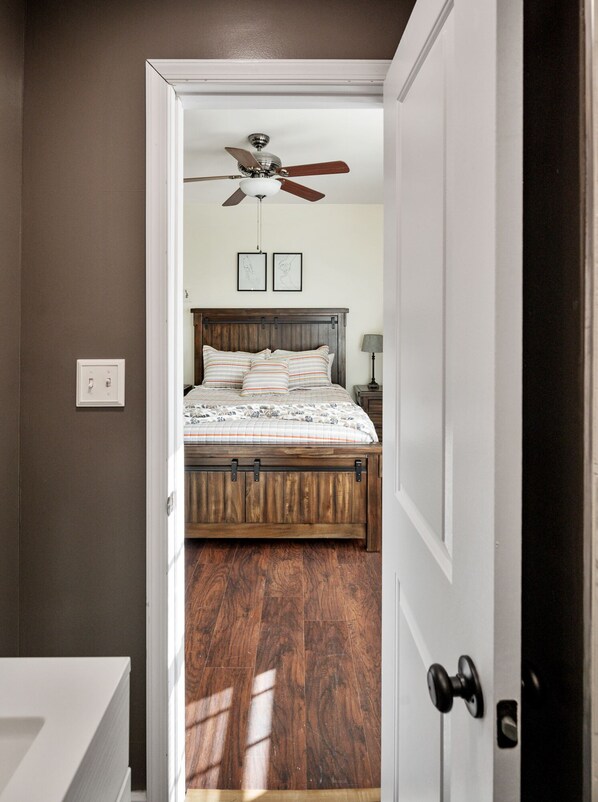 Un dormitorio con cama de madera, ventilador de techo y mesita de noche con lámpara.