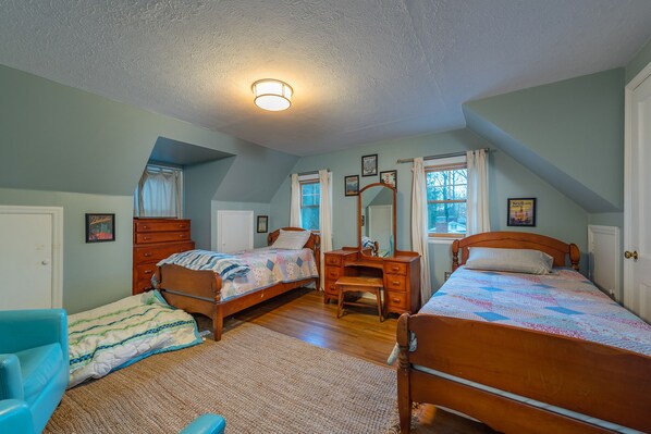 A bedroom with two wooden beds, a dresser, a mirror, and a ceiling light.