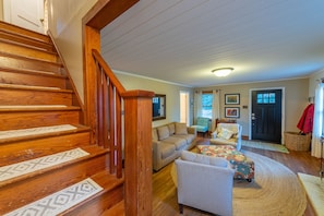 A wooden staircase leading to a living area with a sofa, armchairs, and a patterned rug.