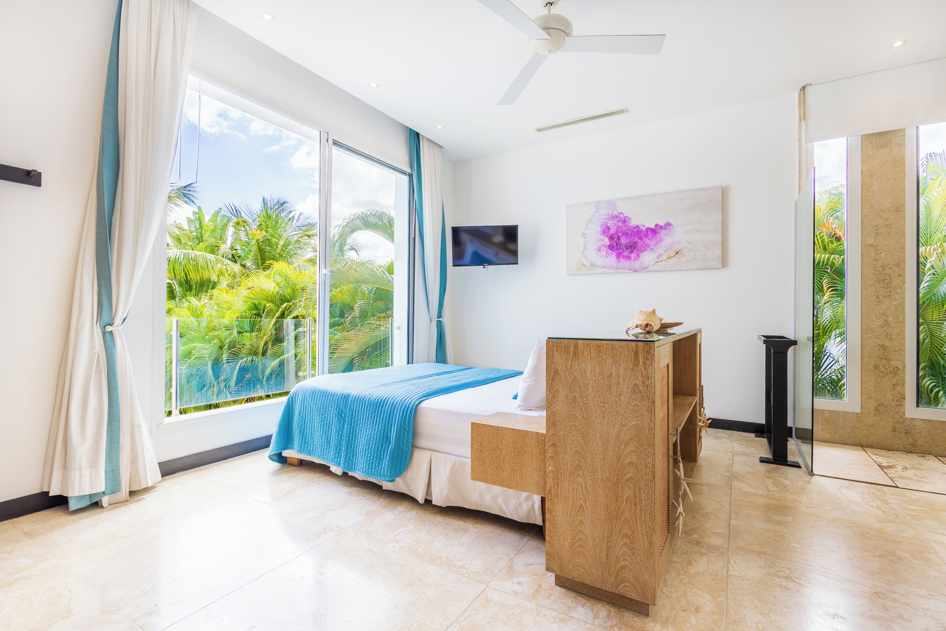 Un dormitorio moderno con cama, escritorio, televisor y ventana grande con vistas a zonas verdes.