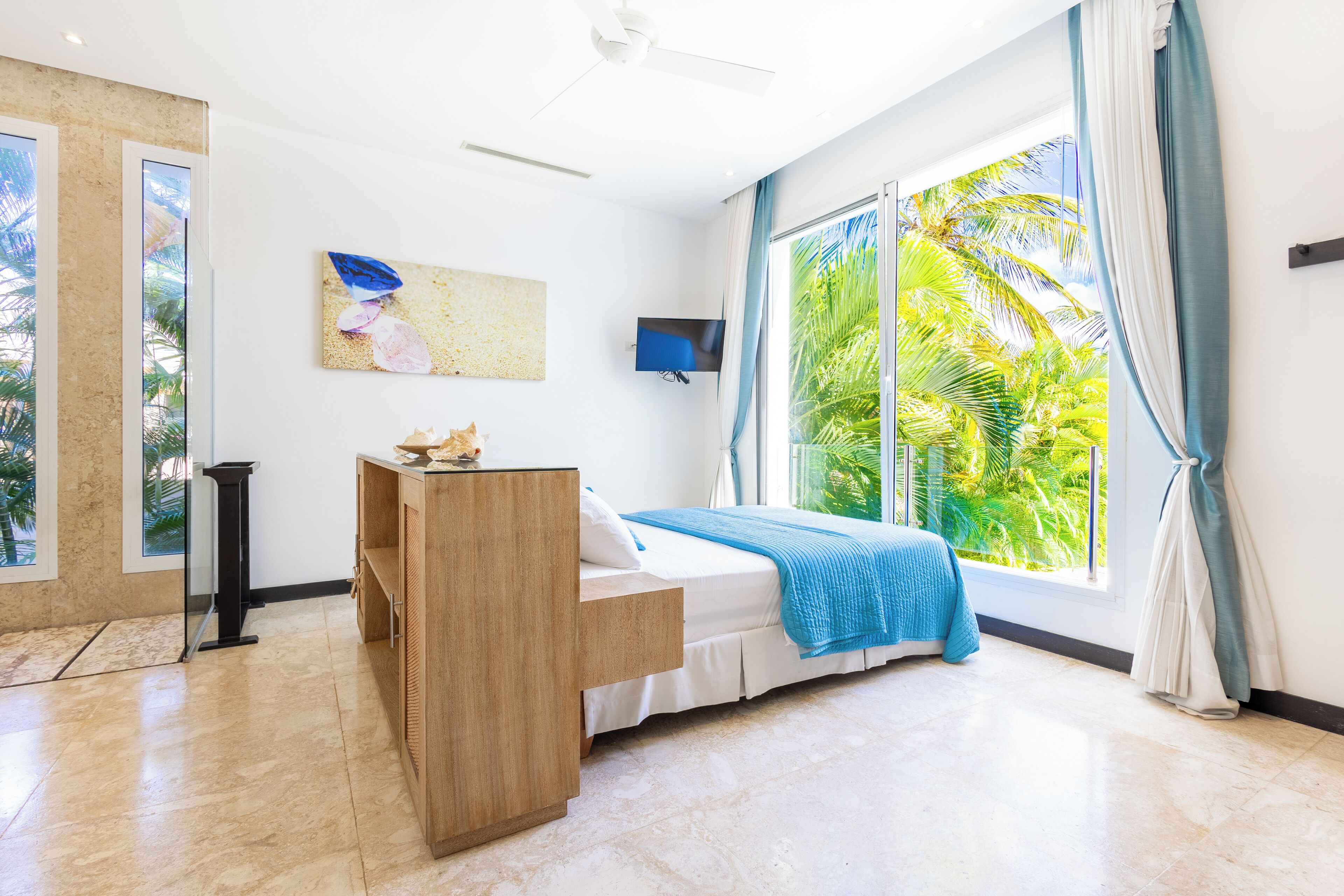 A bedroom with a bed, a wooden nightstand, a TV, and a large window with curtains.