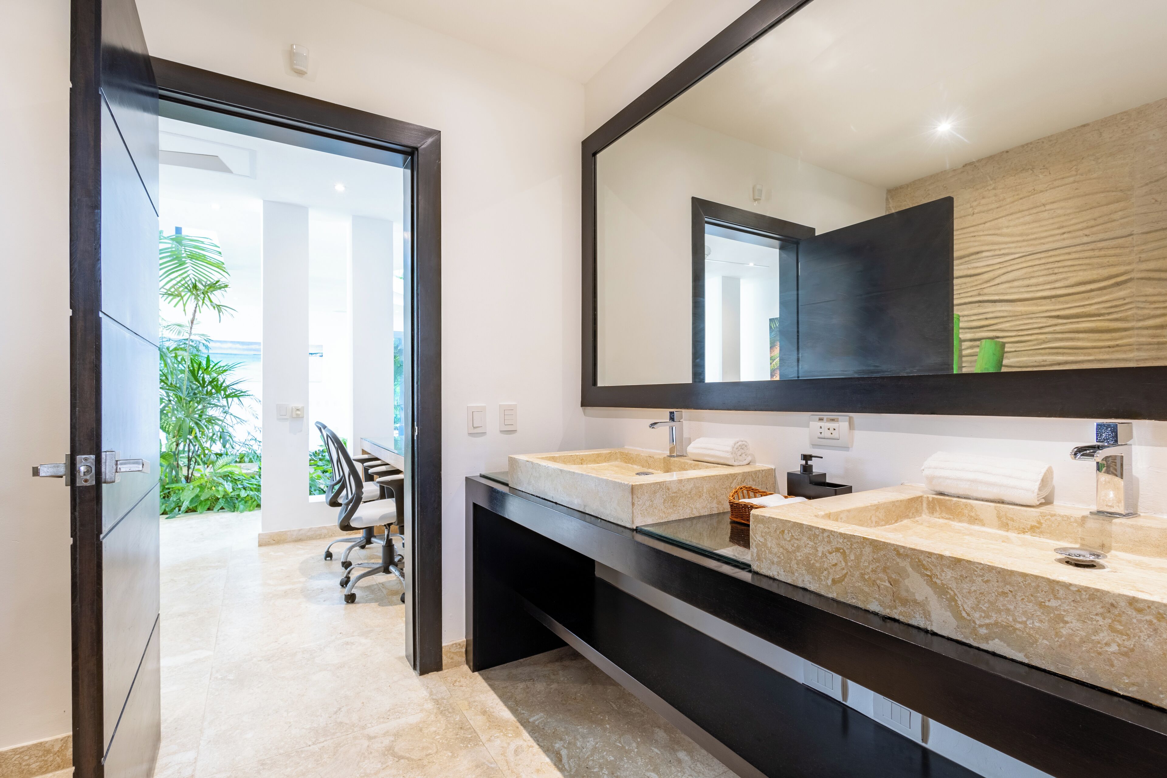 A modern bathroom with two sinks, a large mirror, and a view of a green outdoor area.