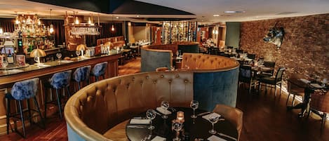 Un restaurante con mesas redondas, asientos de bar y una pared de ladrillo.