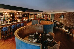 Um restaurante com mesas redondas, bancada de bar e uma parede de tijolos.